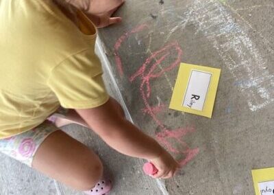 Kid writing on concrete with chalk.